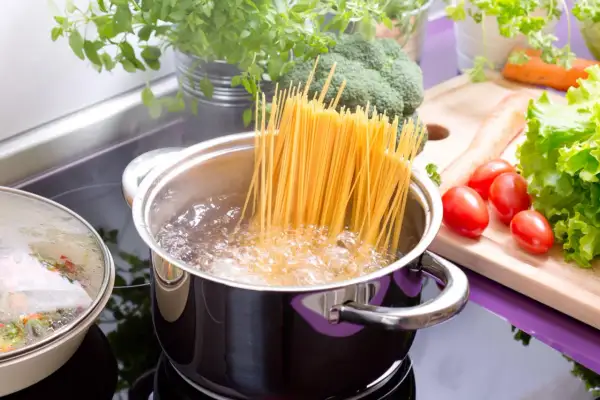Spaghetti kochen in sprudelndem Wasser. Frisches Gemüse wie Brokkoli, Karotten und Tomaten liegen bereit für eine leckere Mahlzeit.