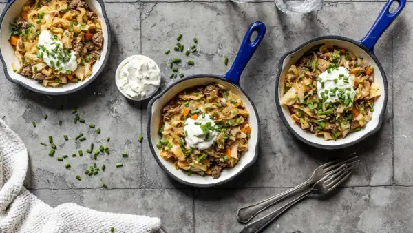 Herzhafte spitzkohl rezepte mit hackfleisch, garniert mit einem Klecks Sauerrahm und Schnittlauch, serviert in kleinen Pfannen.