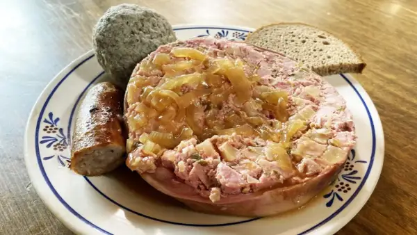 Saumagen-Rezept: Ein deftiger Saumagen mit Zwiebeln, Bratwurst und Brot auf einem Teller.