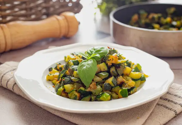 Herzhafte zucchini pfanne, frisch zubereitet und mit Basilikum garniert, serviert auf einem weißen Teller.
