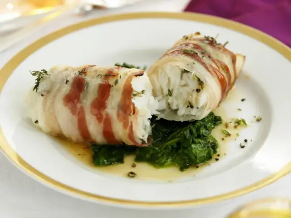 Zwei Fischröllchen, in Speck gewickelt, auf Spinatbett. Ein festliches Gericht, perfekt für Fischgerichte an Weihnachten.