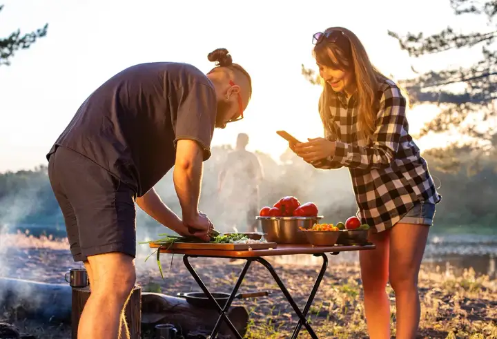 Ein Paar bereitet draußen Gemüse zu, während die Sonne untergeht. Sie kochen im Wohnmobil und genießen die Natur.
