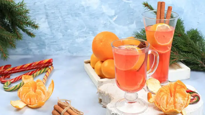 Zwei Gläser mit einem heißen Aperol-Getränk, garniert mit Orangen und Zimt. Daneben Mandarinen, Zuckerstangen und Tannenzweige.